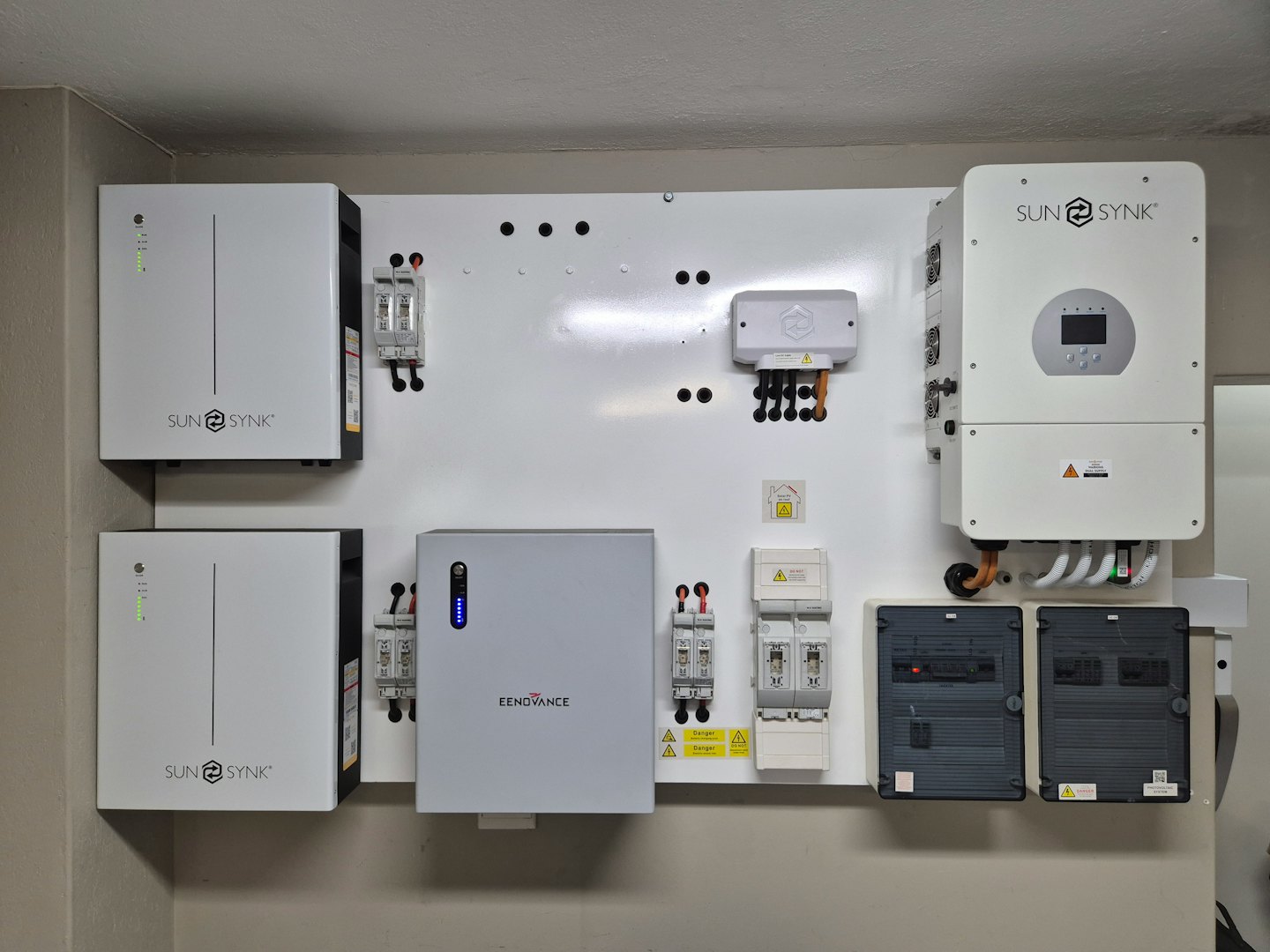 Sistema de energía para el hogar con baterías e inversores en una pared blanca.